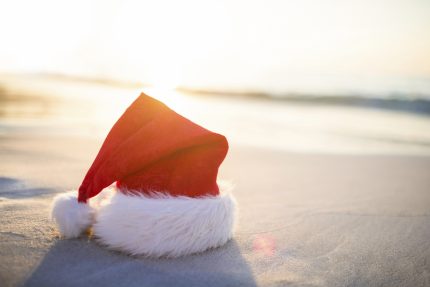 Seasonal Santa hat sitting on beach with sun setting