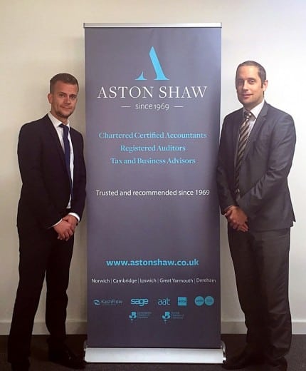 Two newly appointed Aston Shaw directors standing beside the company logo