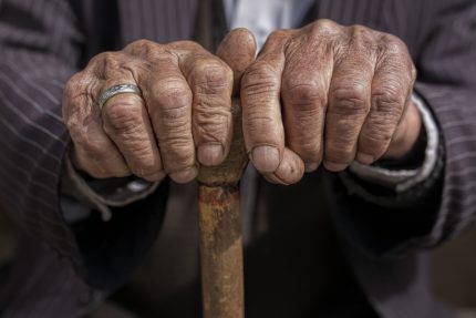 Old aged pensioner holding a cane in between his hands