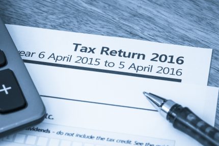 Tax return 2016 document on wooden table with calculator and pen sat on top