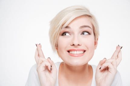 Closeup portrait of a smiling woman with fingers crossed gesture isolated on a white background